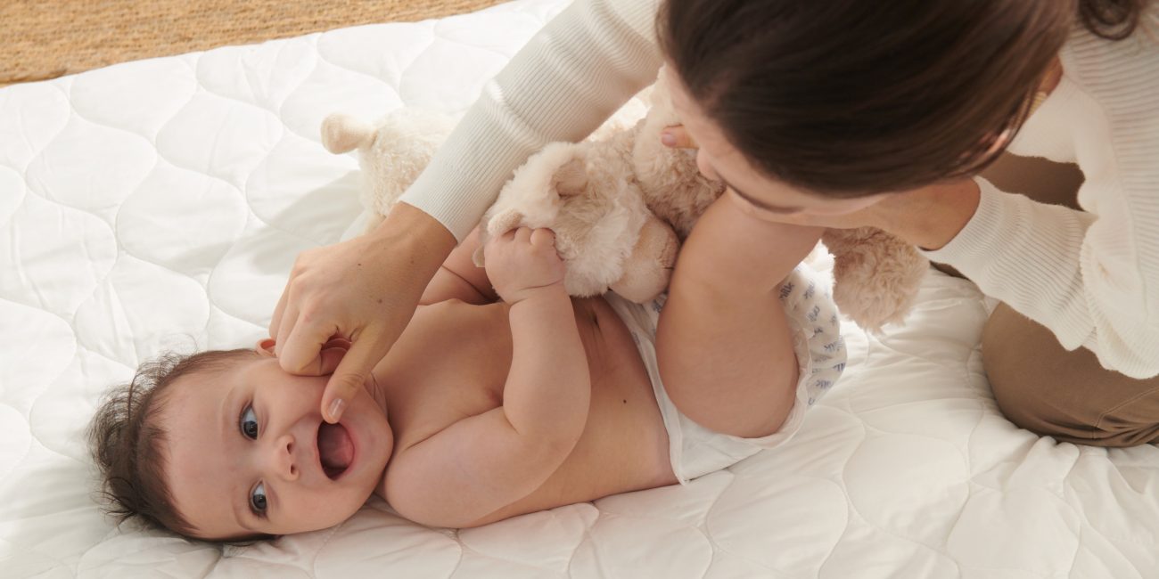 A smiling happy baby in baby diapers on a comfortable blanket with mother playing