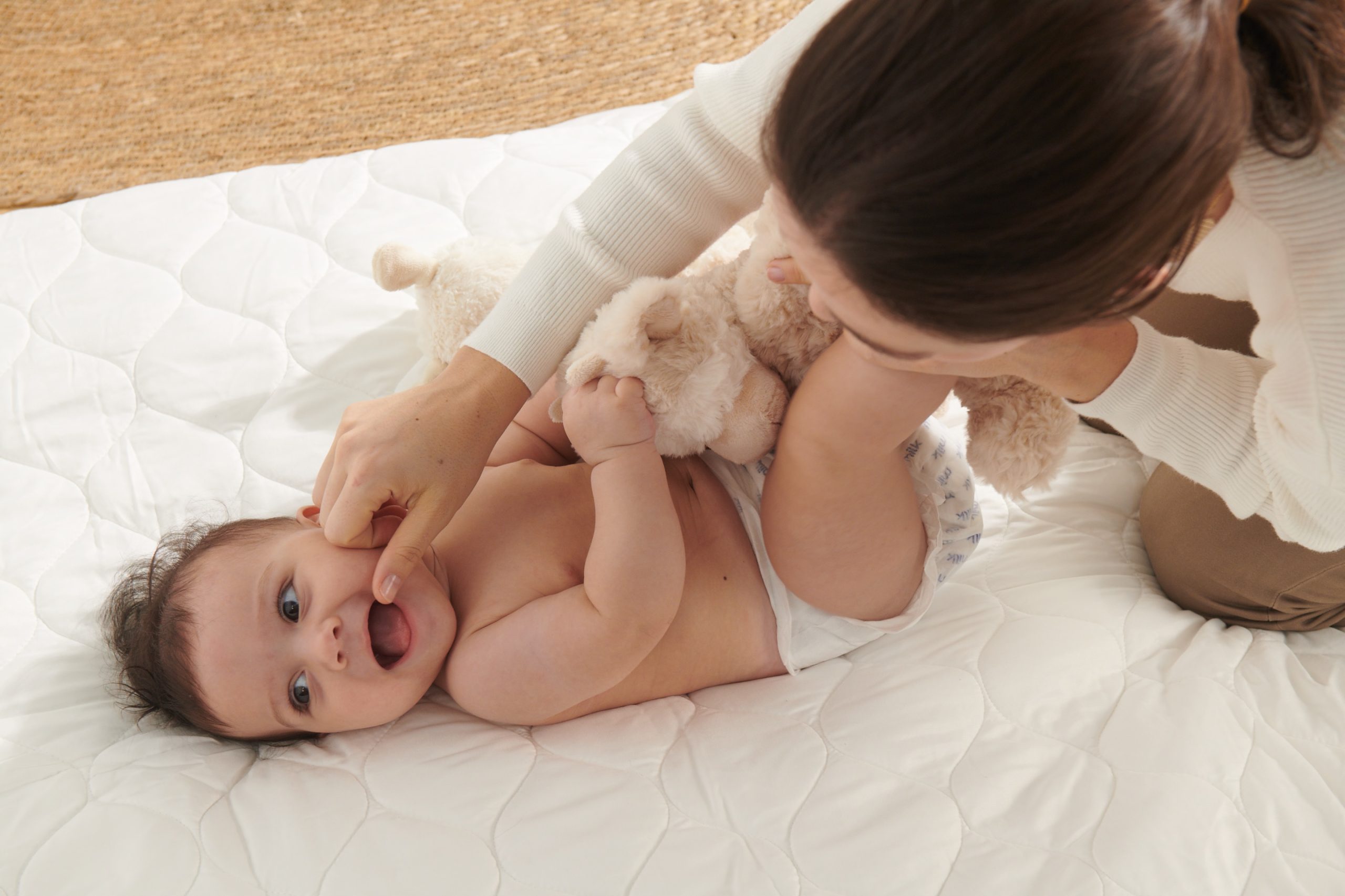 A smiling happy baby in baby diapers on a comfortable blanket with mother playing