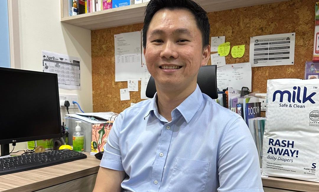 A male doctor seated at a desk, with a baby diaper packaging beside him