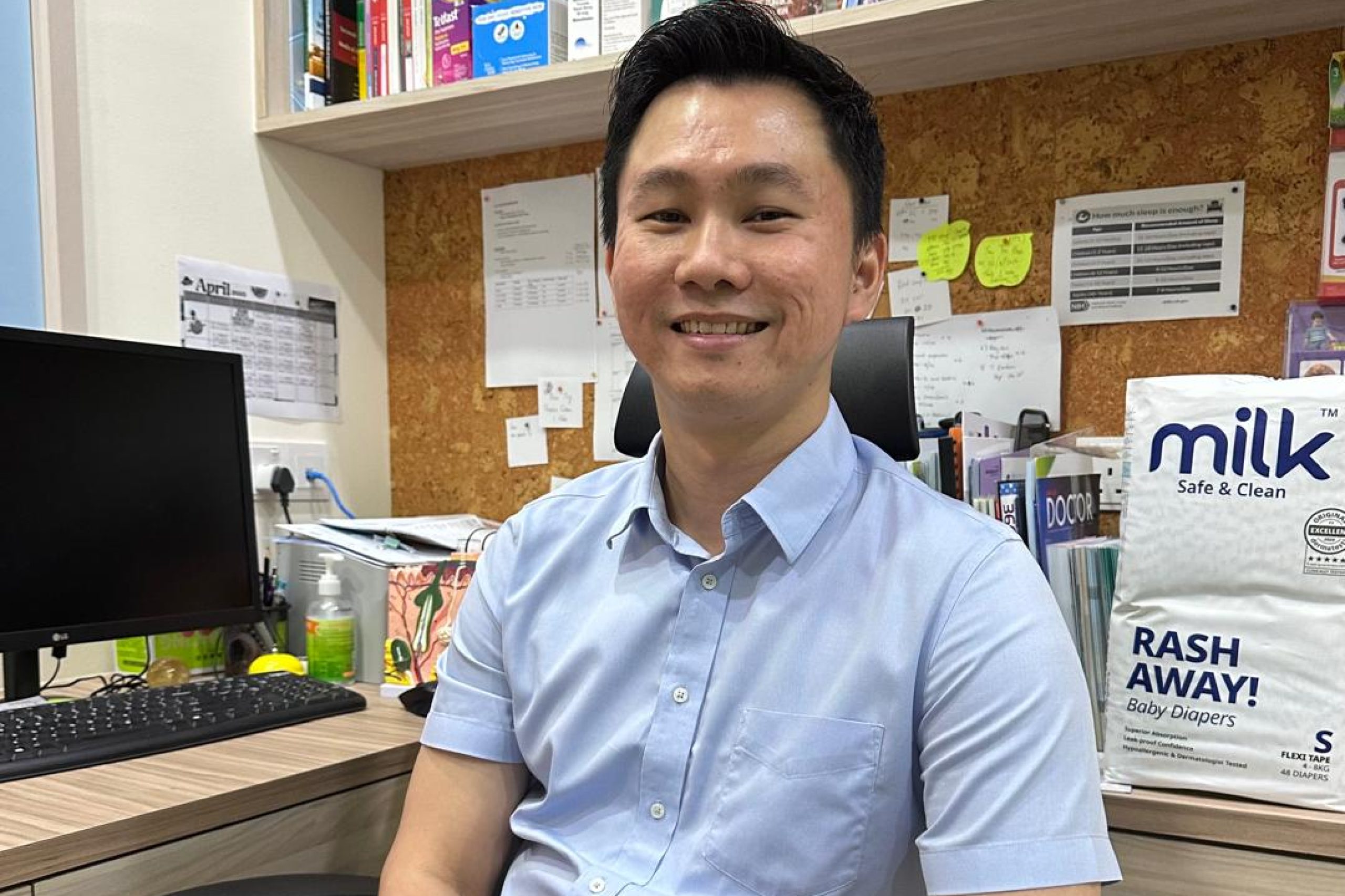 A male doctor seated at a desk, with a baby diaper packaging beside him