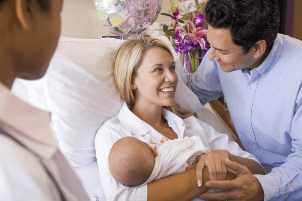 In a hospital room, a man and woman lovingly cradle their baby, capturing a moment of new parenthood.