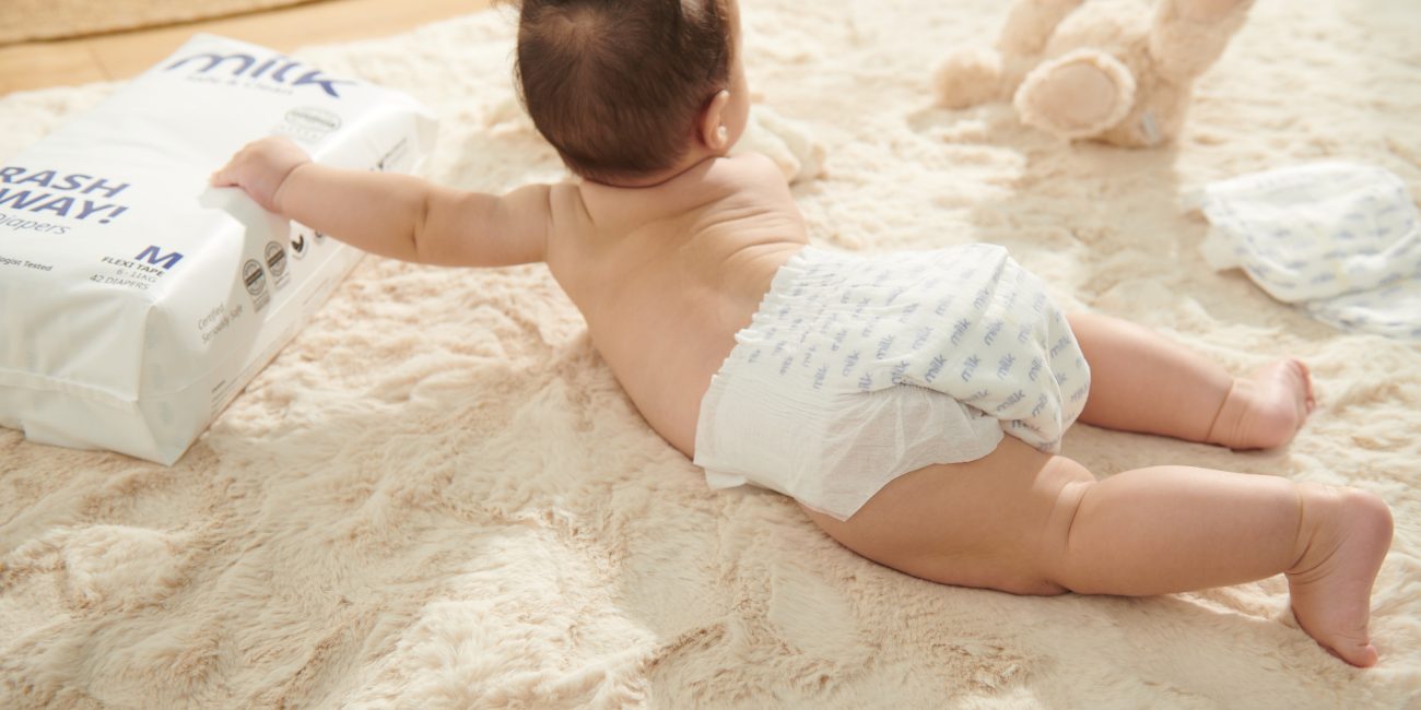 An OEKO-TEX certified diaper-clad baby is sprawled on a plush rug, enjoying a moment of playfulness.