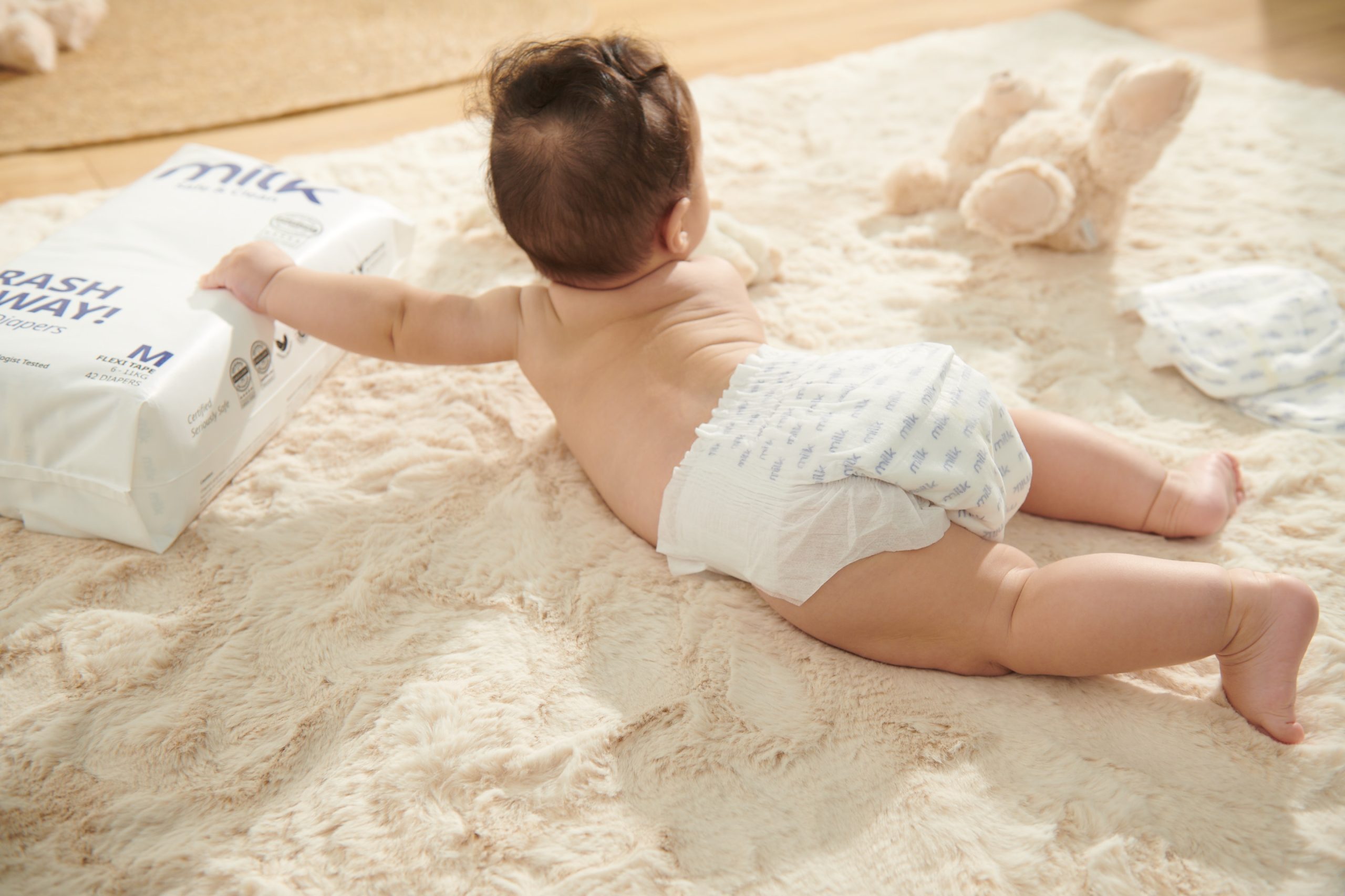 An OEKO-TEX certified diaper-clad baby is sprawled on a plush rug, enjoying a moment of playfulness.