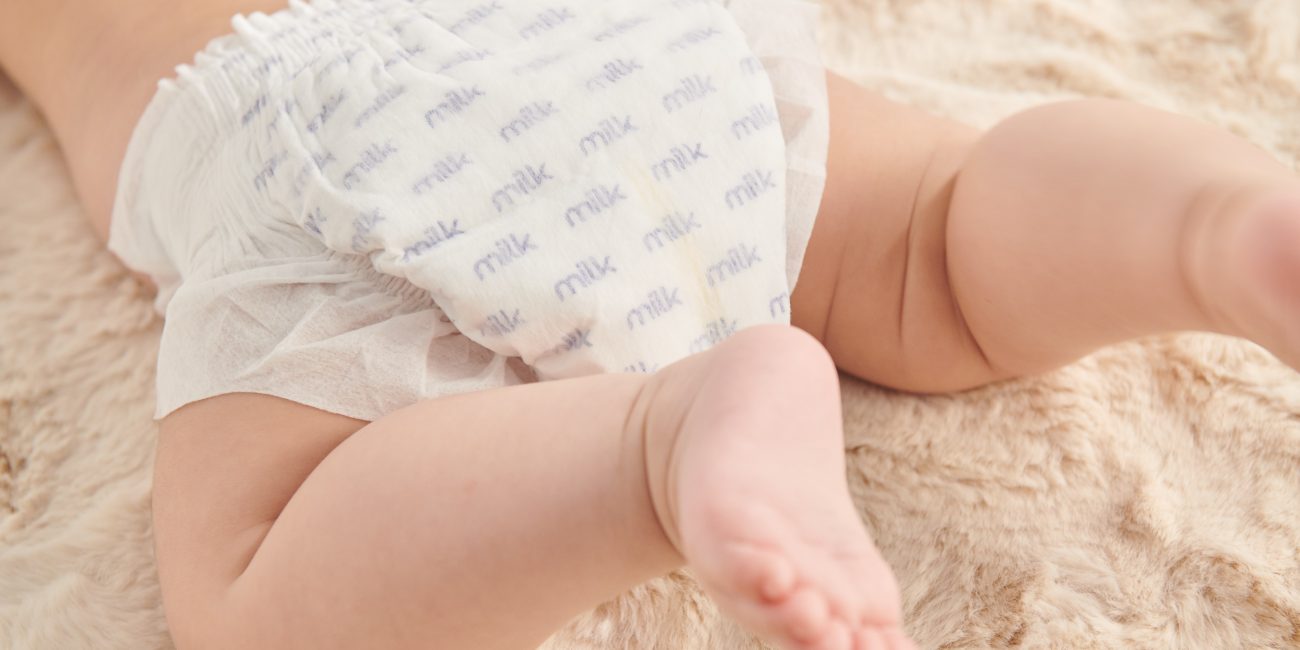 Baby in white diapers with MILK logo on a beige carpet