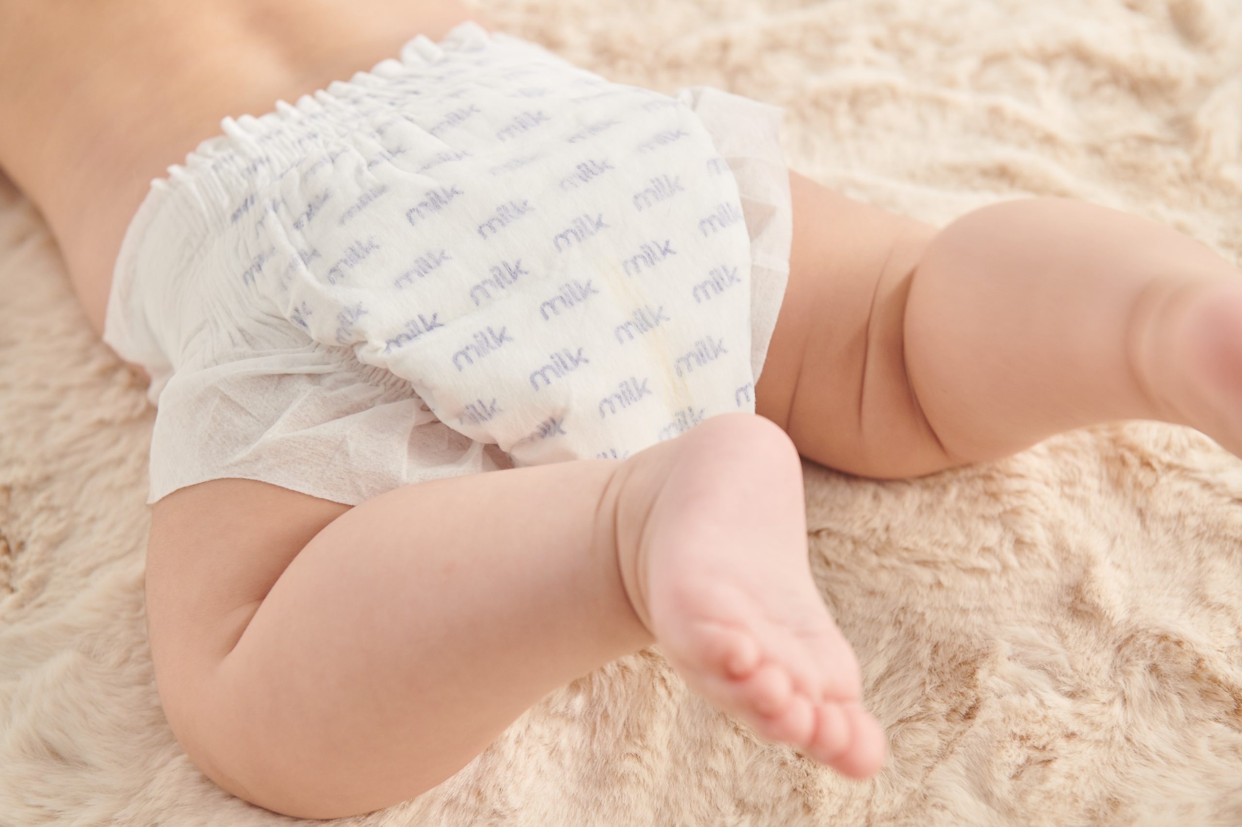 Baby in white diapers with MILK logo on a beige carpet