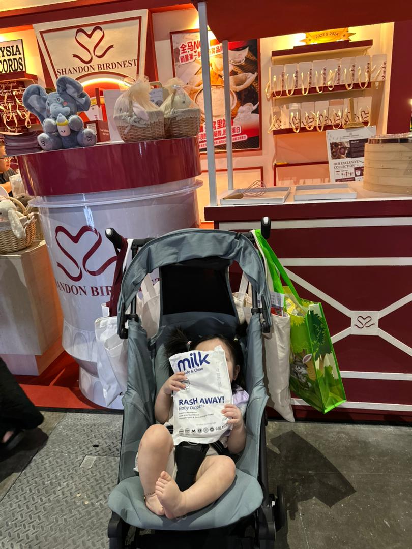 baby holding MILK diaper trial pack in front of a booth
